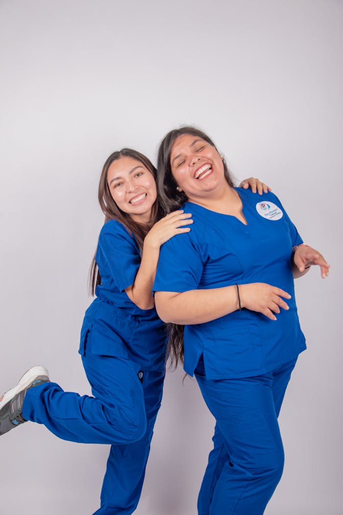 Mastering the First Impression: Your intriguing post title goes here Two smiling nurses in blue uniforms enjoying a joyful moment, showcasing teamwork and positivity.