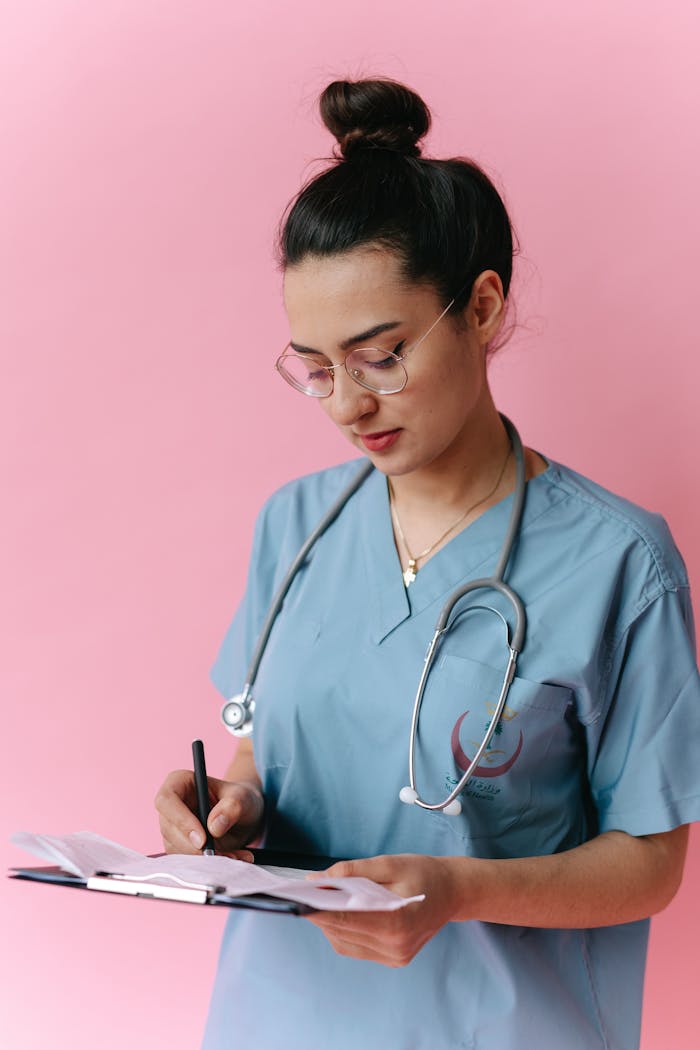 The Art of Drawing Readers In: Your attractive post title goes here Portrait of a young nurse in scrubs writing medical notes on a clipboard against a pink background.